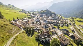 Luftaufnahme des Dorfes Ardez im Engadin mit Burgruine Steinsberg und umliegender Alpenlandschaft.