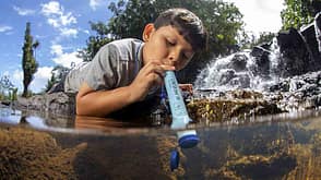 Junge der einen LifeStraw® Personal von Vestergaard in einem Fluss benutzt Junge der einen LifeStraw® Personal von Vestergaard in einem Fluss benutzt