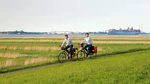 Pärchen radelt am Deich, Containerschiff im Hintergrund 