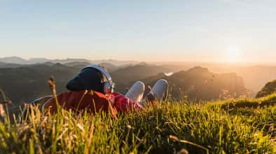 Hiker lying in grass, taking a break and listening music with headphones