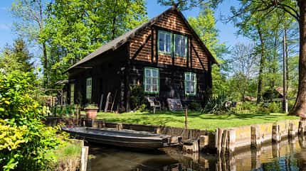 Spreewald,Spree,Fließ,Urlaub,Reise,Lehde,Lübbenau,Haus,Gebäude,Bäume,Wald,Fluß,Natur,Landschaft,Brandenburg,Architektur,Dorf,Sehenswürdigkeit,Boot,Kahn,Holzkahn,Spreewaldkahn,grün,alt,historisch,Tradition,Reiseziel,erholen,entspannen,Erholung,Idylle,romantisch,Tourismus,Querformat,Deutschland,Wasser,Ufer,Uferbefestigung,Frühling Gebäude im Spreewald in Lehde