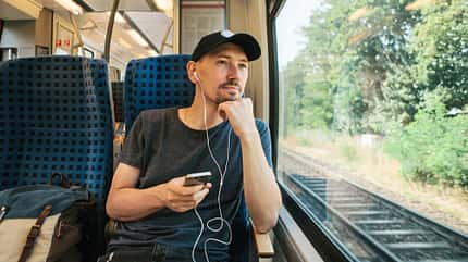 Reisen mit der Bahn - Mann mit Kopfhörern und Rucksack Reisen mit der Bahn - Mann mit Kopfhörern und Rucksack