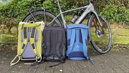 Radtaschen-Rucksack-Hybride von Deuter, Vaude und Thule in der Vergleichsansicht neben Fahrrad