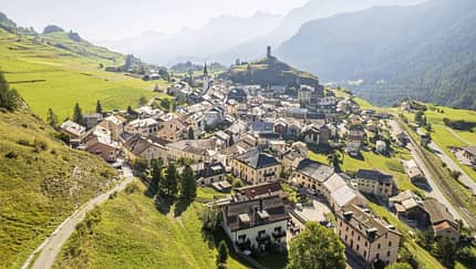 Luftaufnahme des Dorfes Ardez im Engadin mit Burgruine Steinsberg und umliegender Alpenlandschaft.