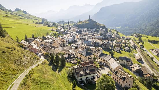 Luftaufnahme des Dorfes Ardez im Engadin mit Burgruine Steinsberg und umliegender Alpenlandschaft.